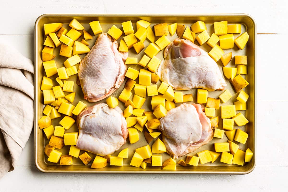 Diced potatoes and chicken thighs on a cookie sheet.