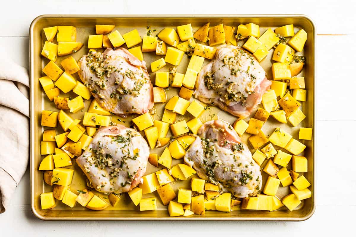 Chicken thighs and potatoes with garlic butter over the top on a cookie sheet.