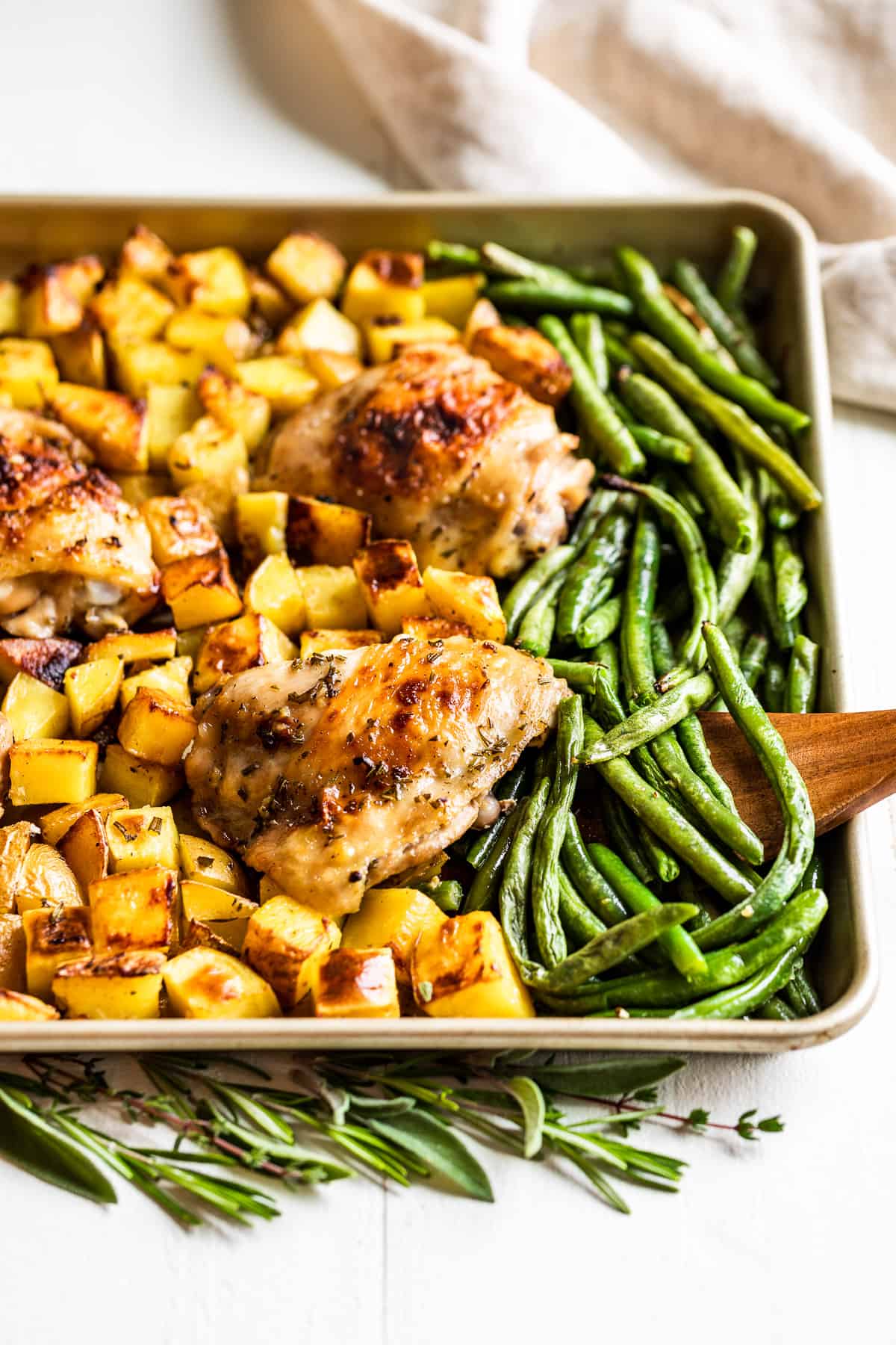 Garlic Butter Chicken with roasted potatoes and green beans on a gold baking sheet.