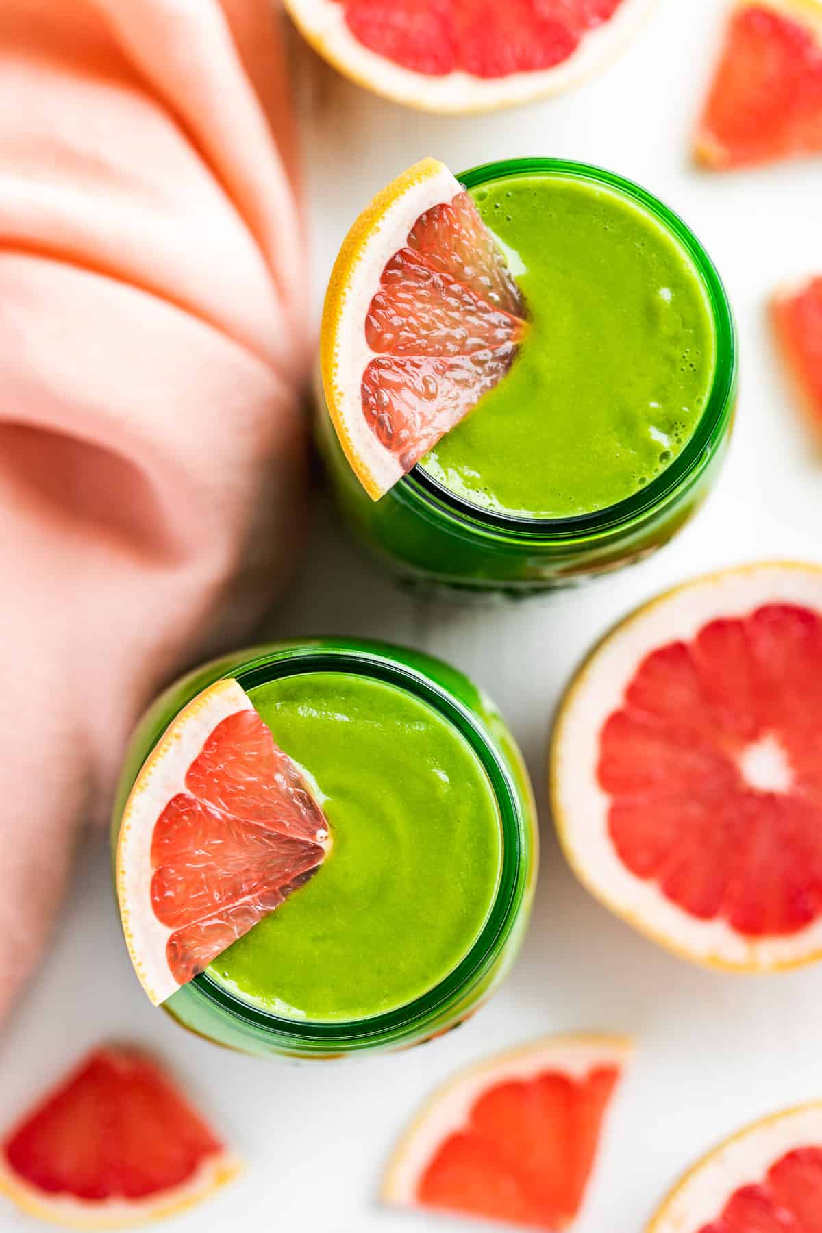 Two green glass jars of Grapefruit Green Smoothie with grapefruit slices around them.