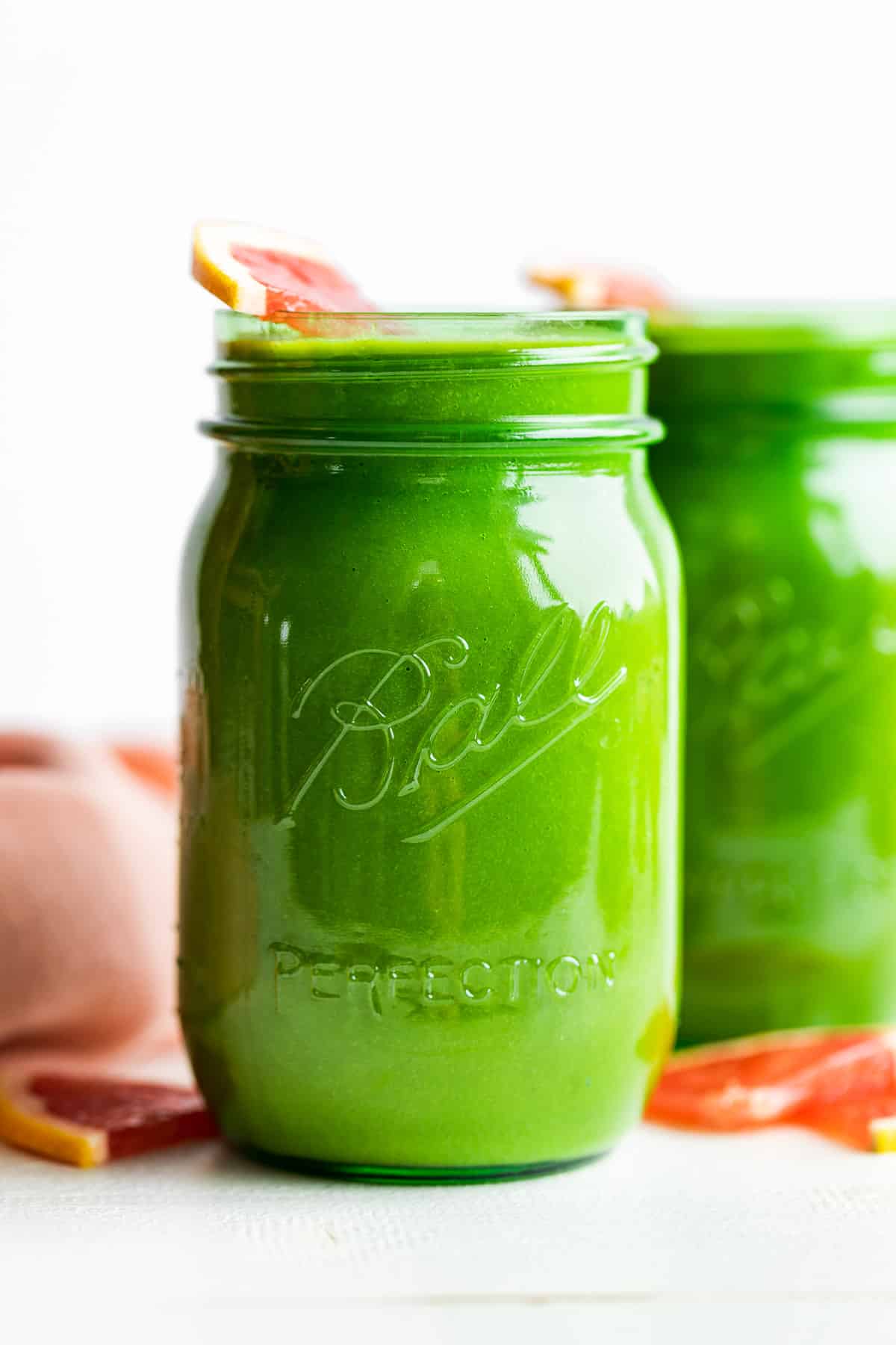 Straight on view of 2 green glass jars of smoothie with grapefruit slices around.