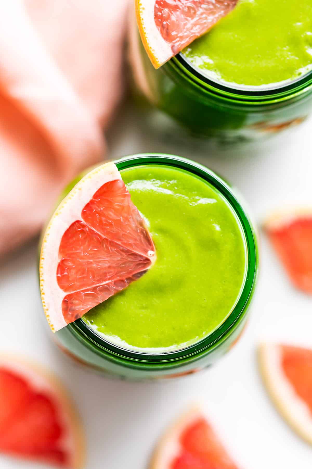 Close view of one green glass jar of Grapefruit Green Smoothie with grapefruit slices around.