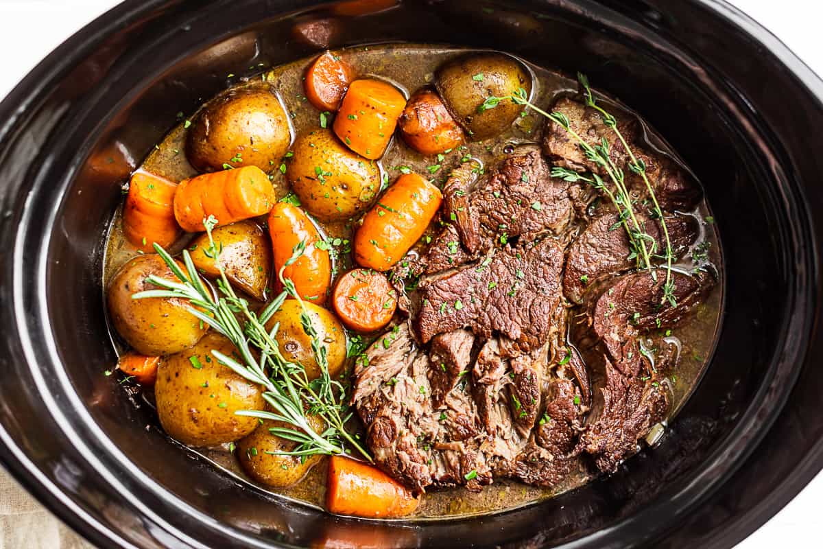 Finished Slow Cooker Pot Roast in the slow cooker bowl with rosemary on top.