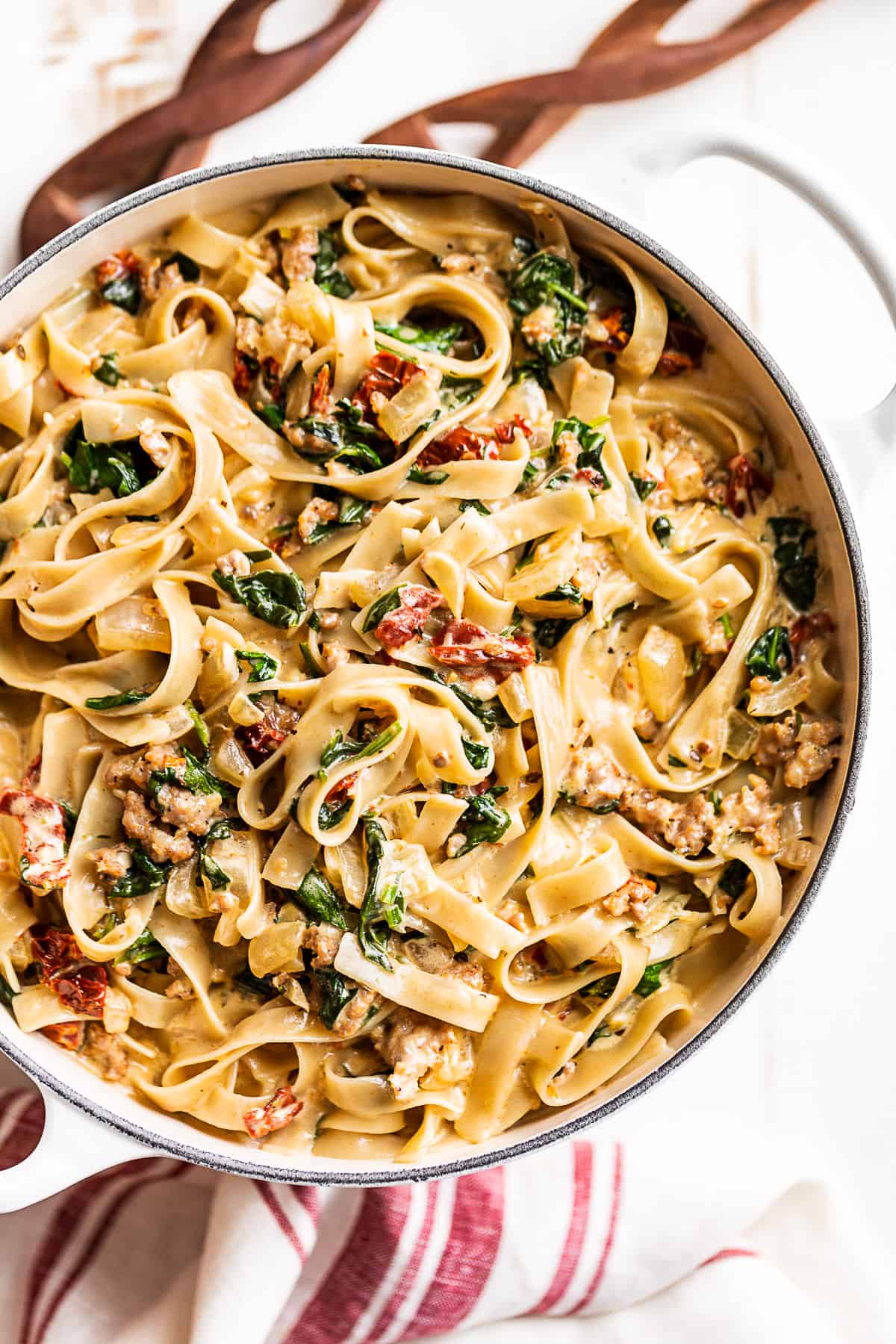 A large white pot filled with Tuscan Sausage Pasta with wooden spoons on the side.