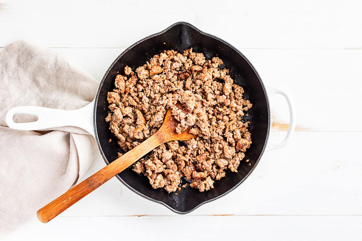 Browned Italian sausage in a white cast iron skillet.