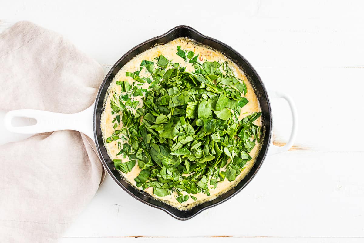 Adding the spinach to the creamy sauce in a white skillet.