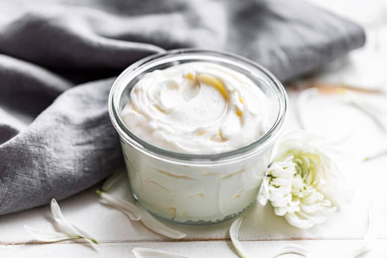 Whipped Body Butter and a glass jar with a grey linen in the background.