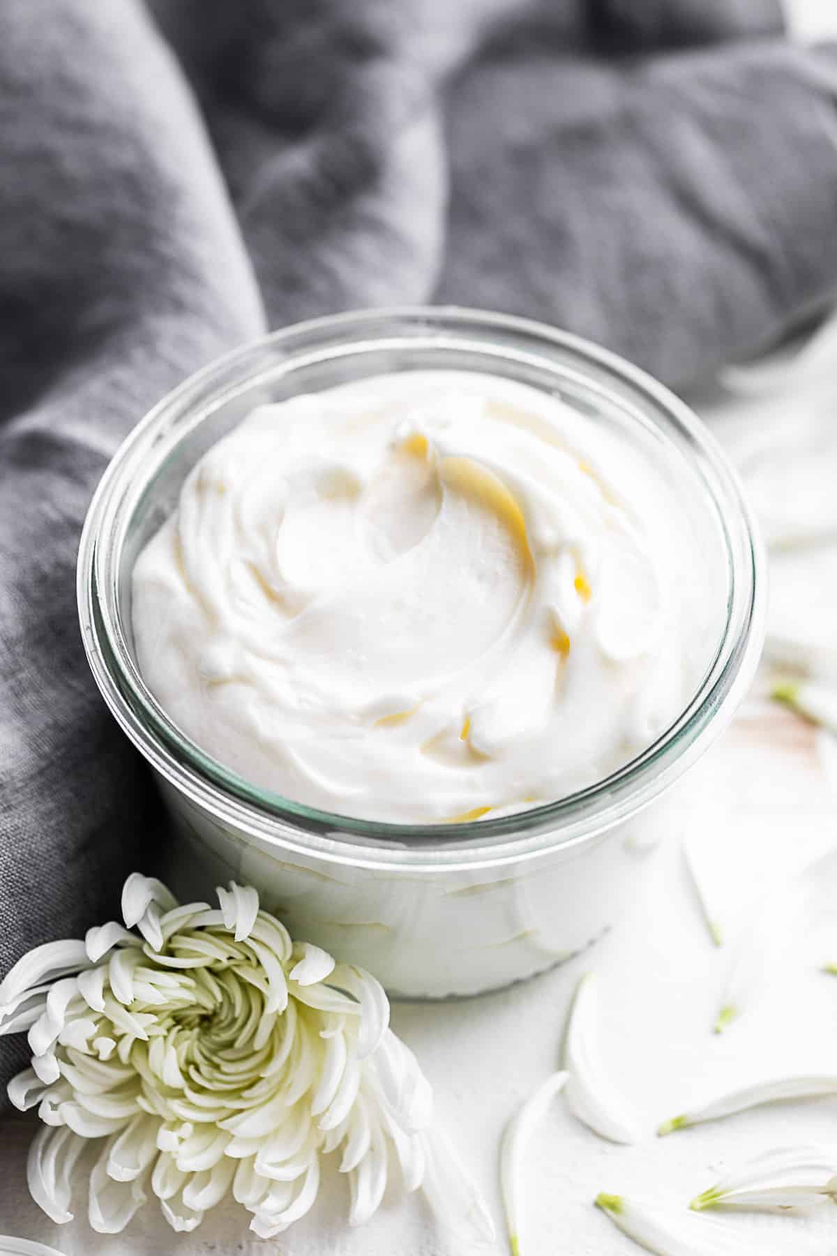 Whipped Body Butter in a glass jar with a white flower in front and petals around it.