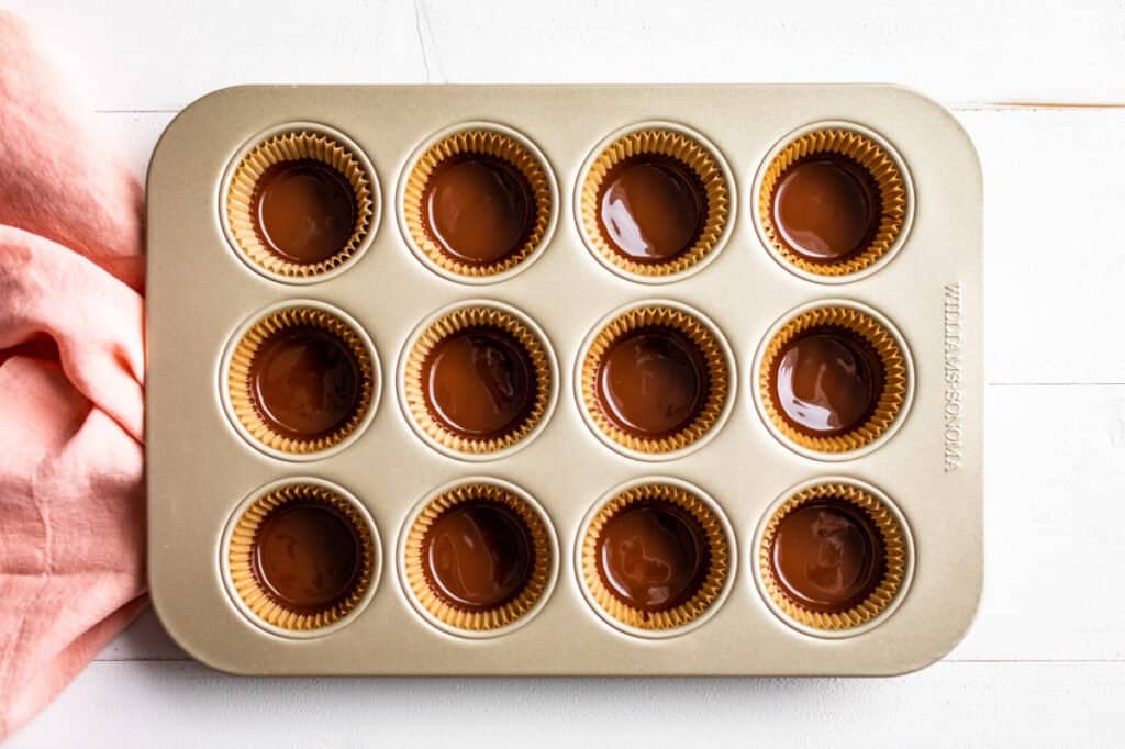 Chocolate coating the bottoms of 12 muffin cup liners in a muffin tin.