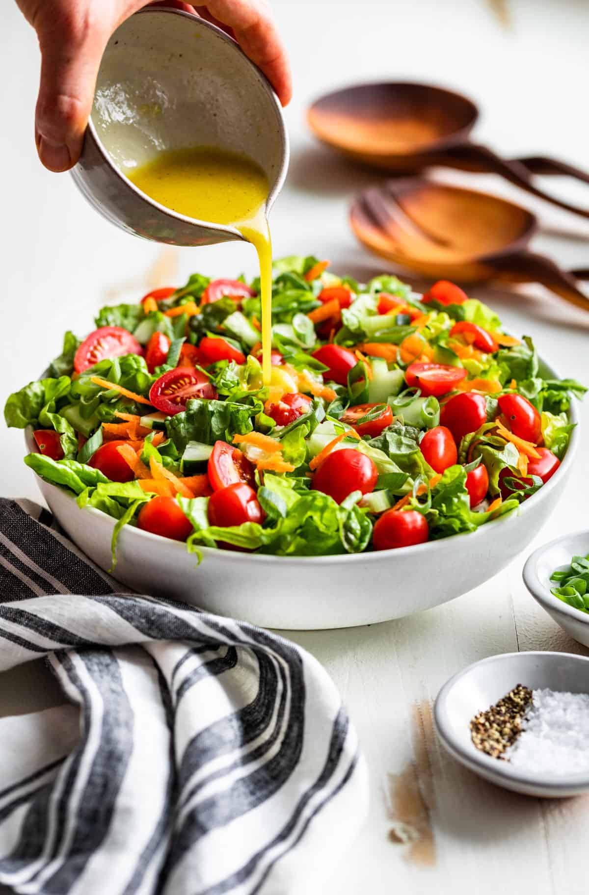 Lemon Vinaigrette being poured over a white bowl filled with Easy Green Salad.