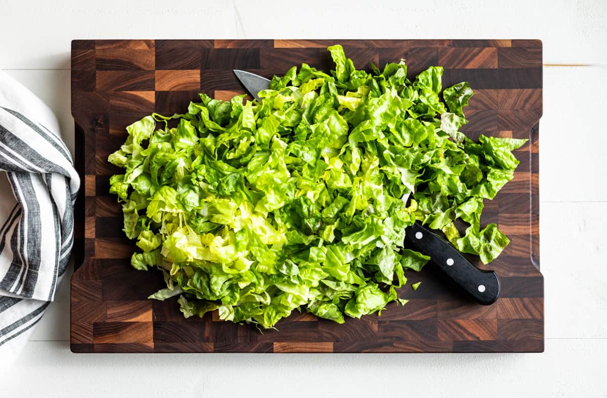 Chopped green leaf lettuce on a wooden cutting board.