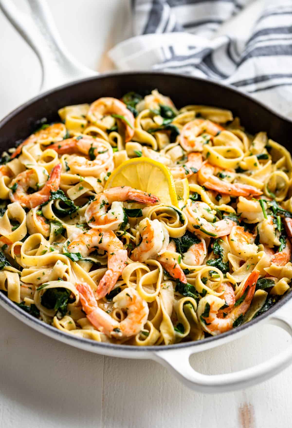 Side view of Garlic Butter Shrimp Pasta in a white skillet topped with a slice of lemon.