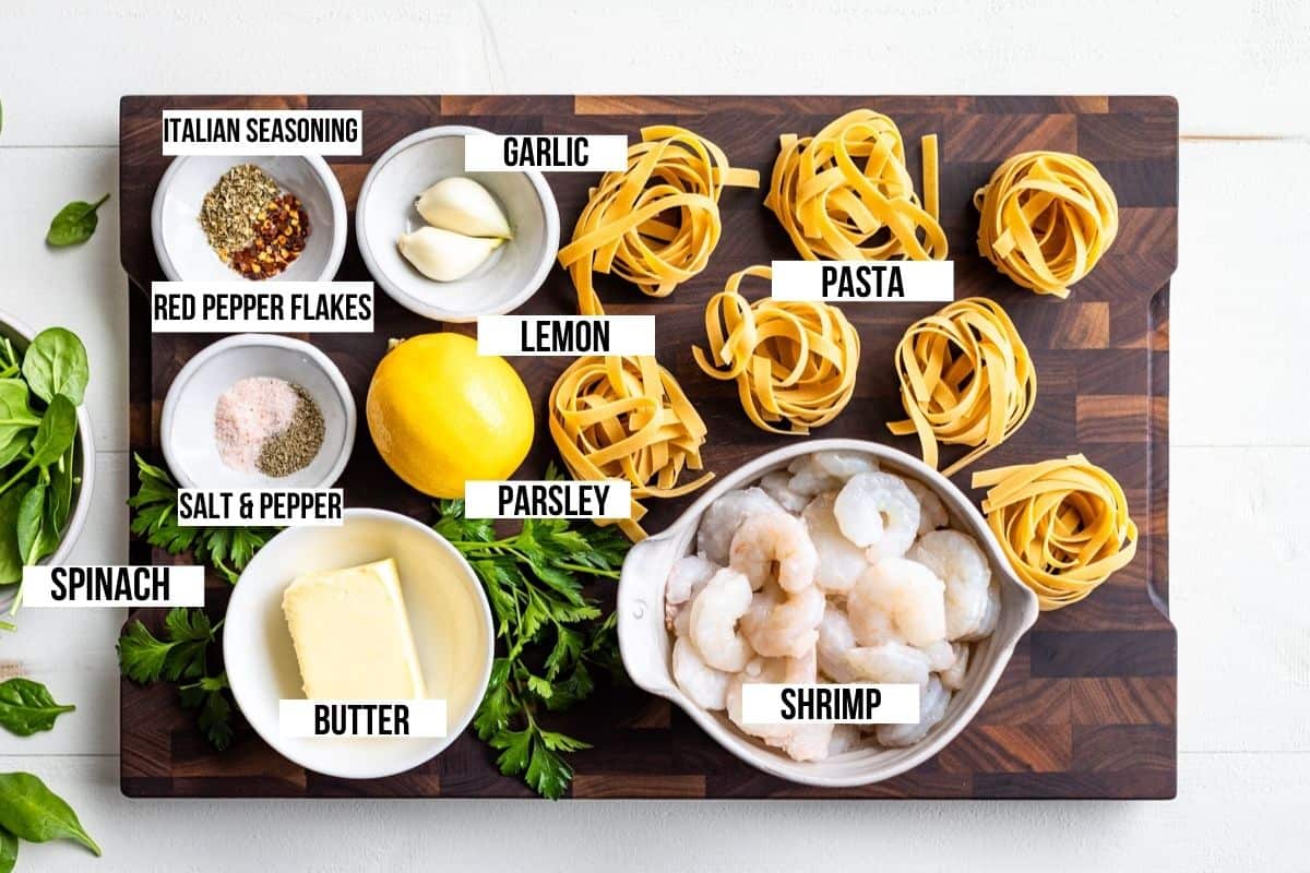 Tagliatelle pasta, shrimp, lemon, butter, garlic, and spices on a wooden cutting board.