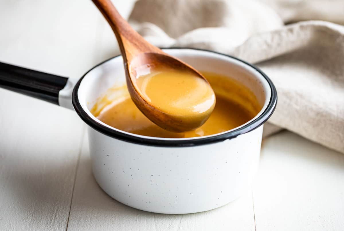 Finished gluten free gravy in a white pot with a wooden spoon scooping some out.