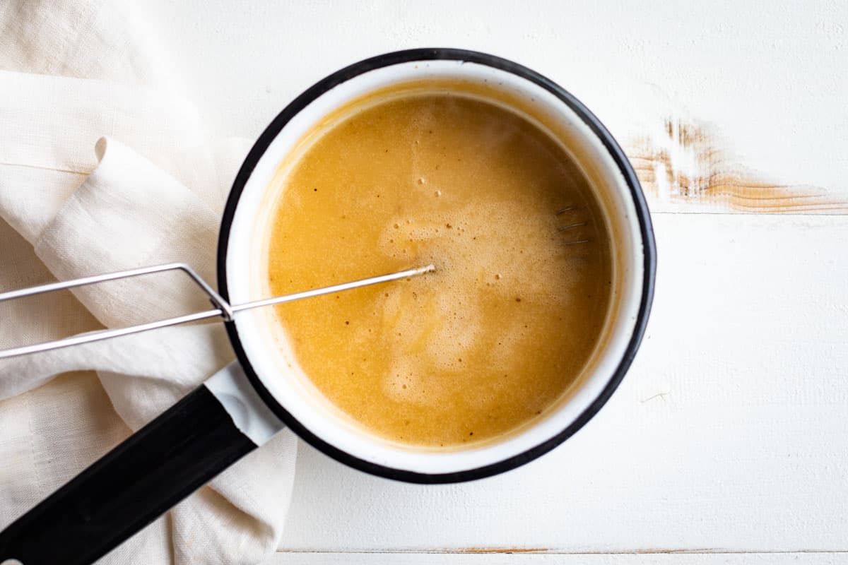 Broth whisked into the roux and cooked to thicken in a small white pot.