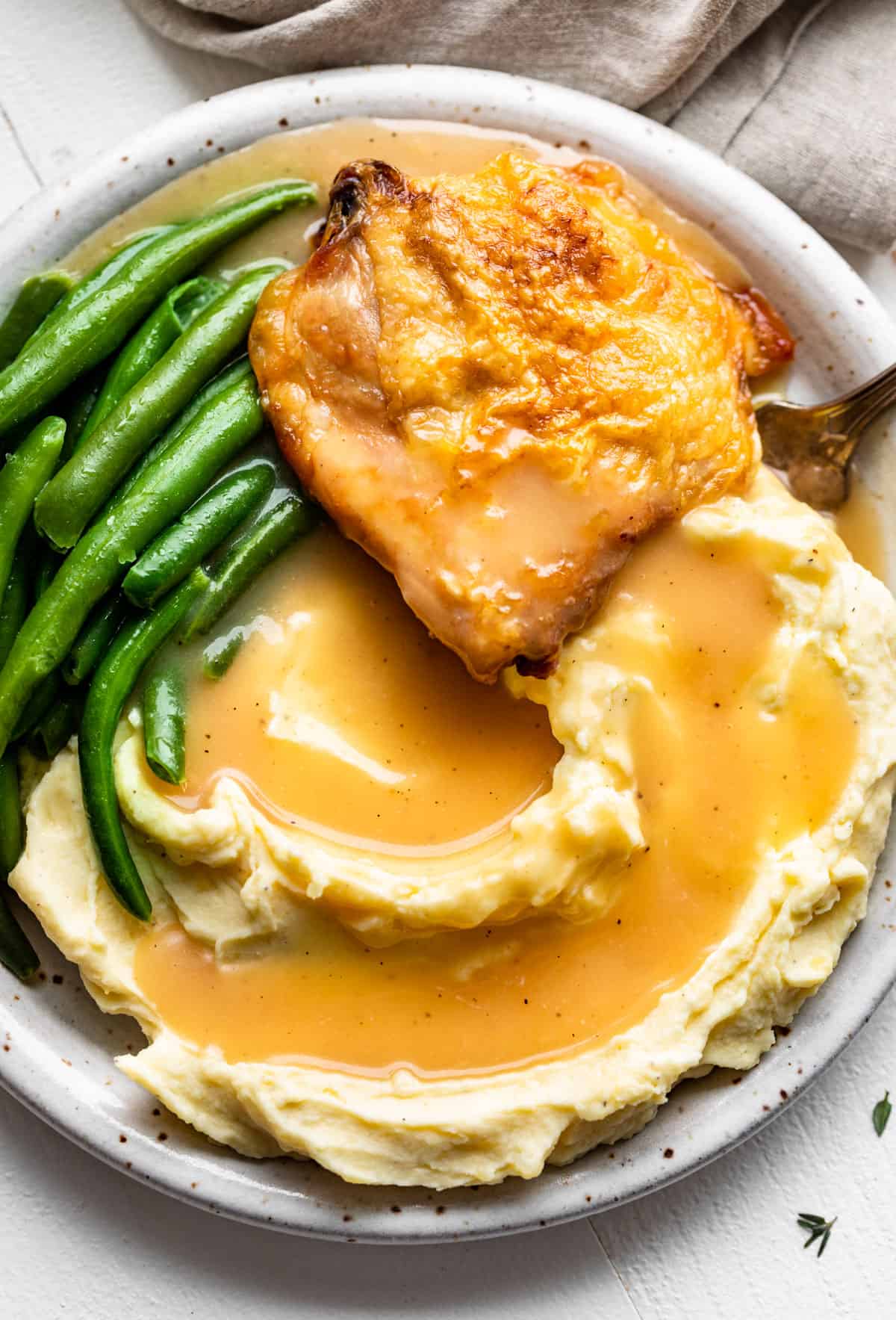 Straight down view of mashed potatoes, chicken, and green beans with gravy poured over the top.
