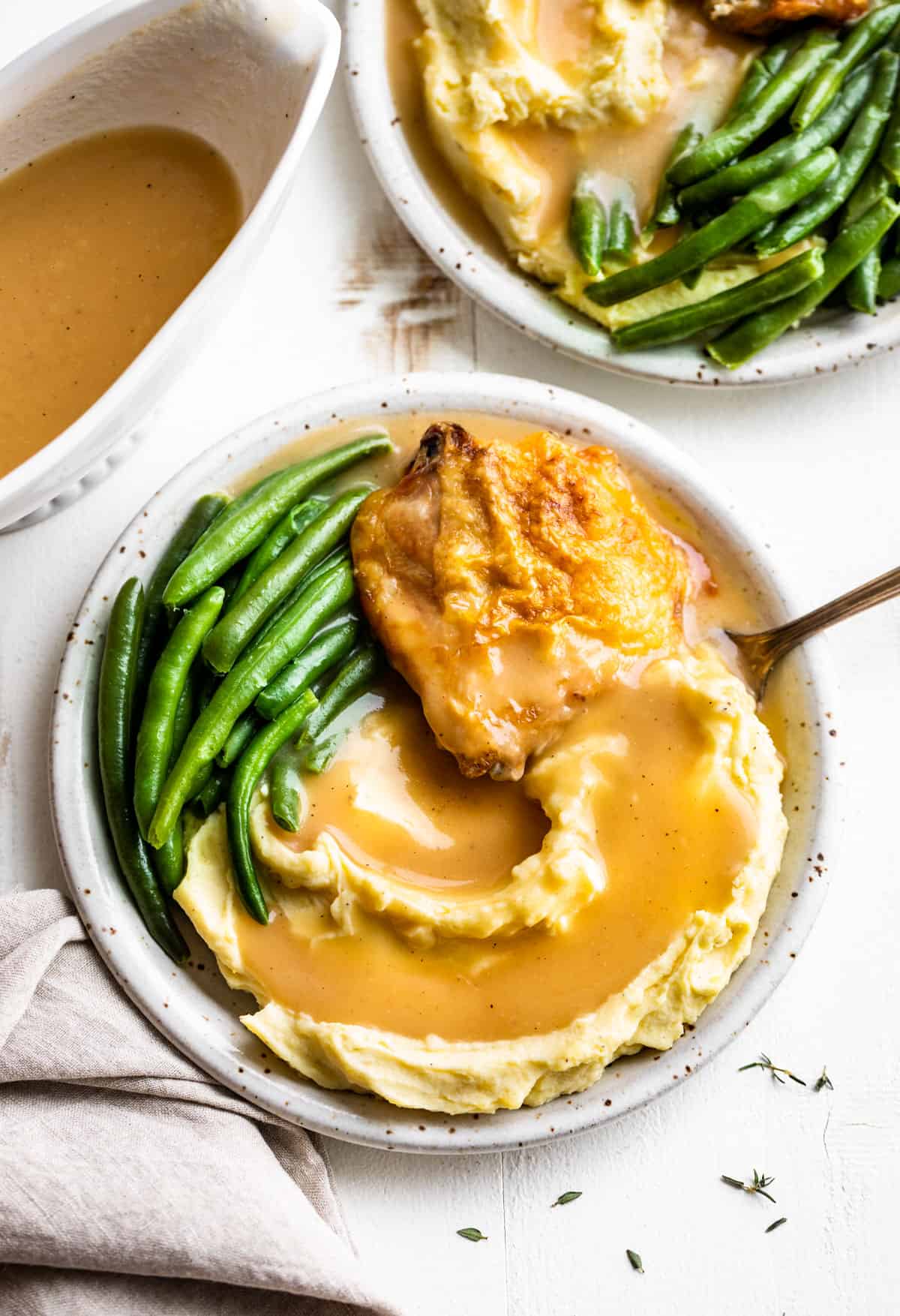 Two plates of mashed potatoes with chicken, green beans, and gravy with a gravy boat on the side.