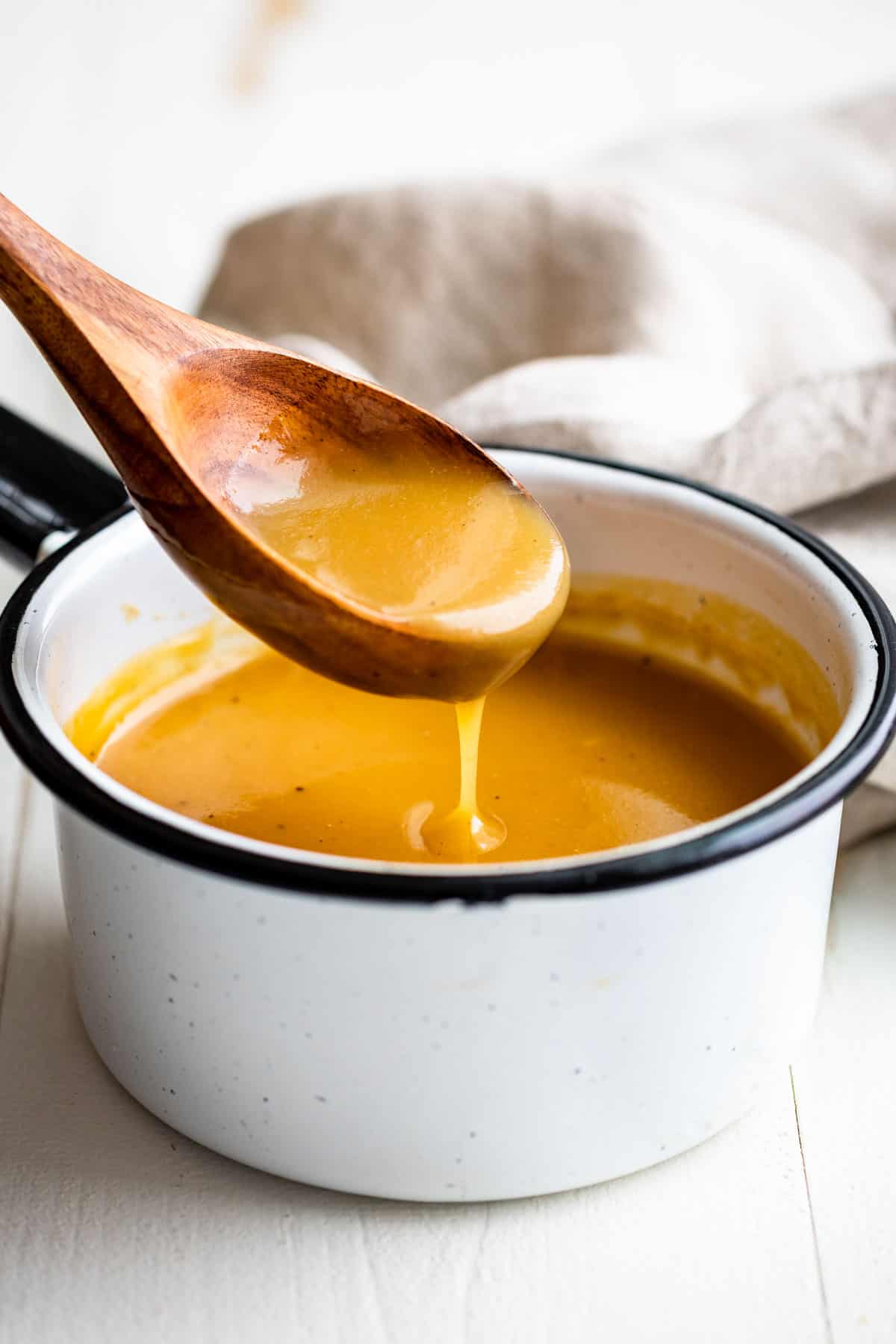 Close side view of Gluten Free Gravy with a wooden spoon scooping some out of the white pan.