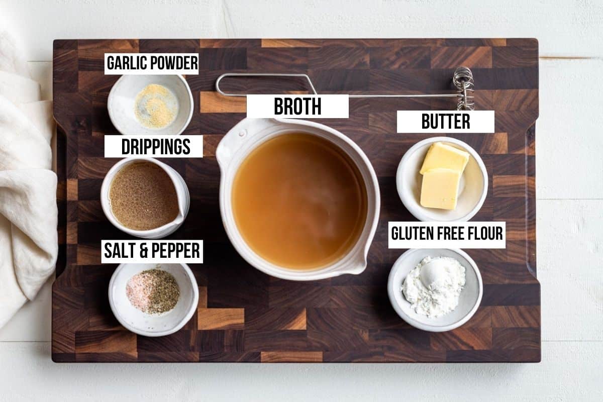 Broth, garlic powder, pan drippings, salt and pepper, gluten free flour, and butter in small bowls on a wooden cutting board.