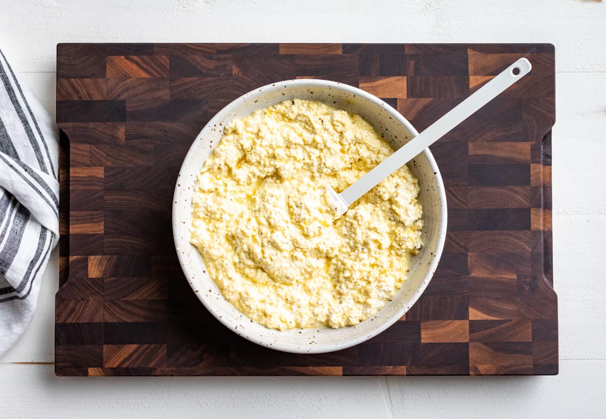 The ricotta mixture for the lasagna in a white bowl on a wooden cutting board.