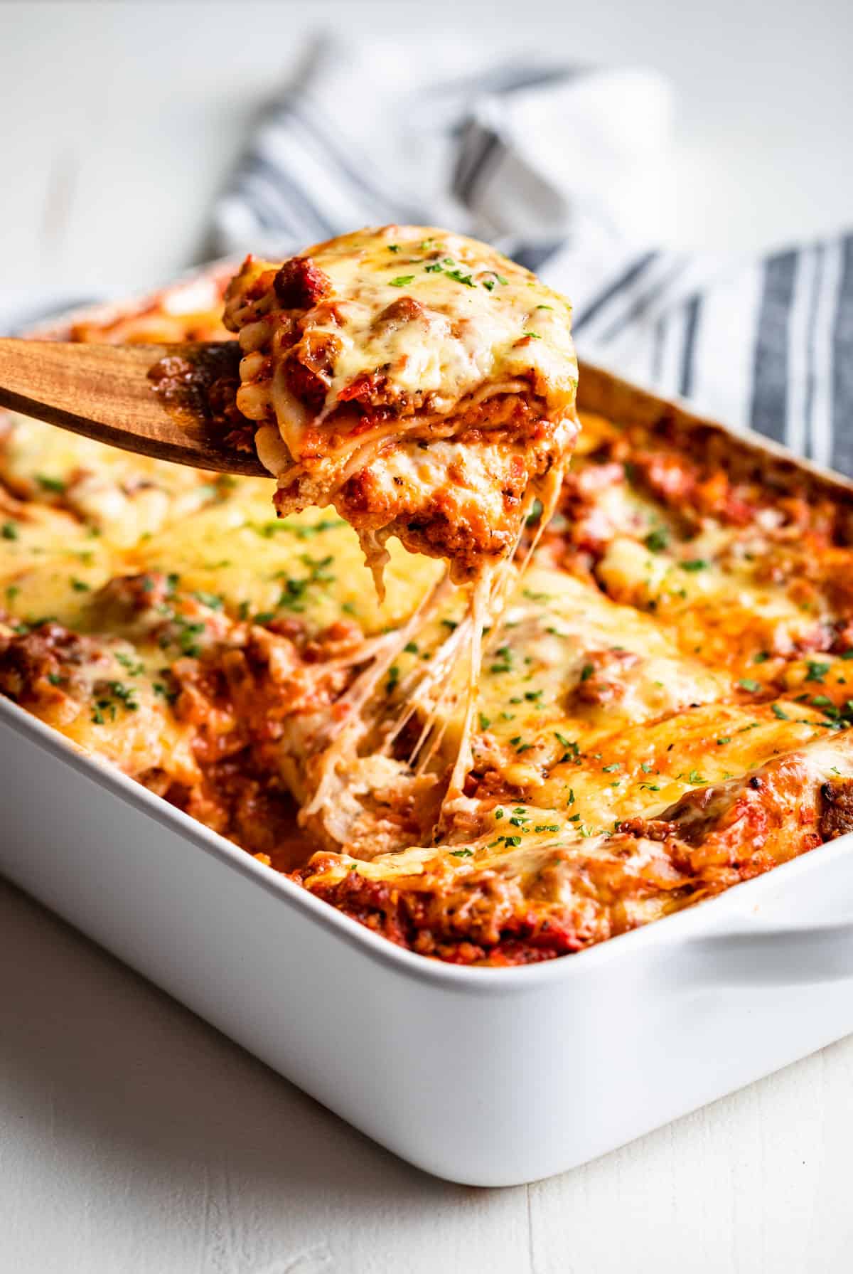 Large white baking dish with lasagna with a large slice being lifted out with strings of cheese coming down.