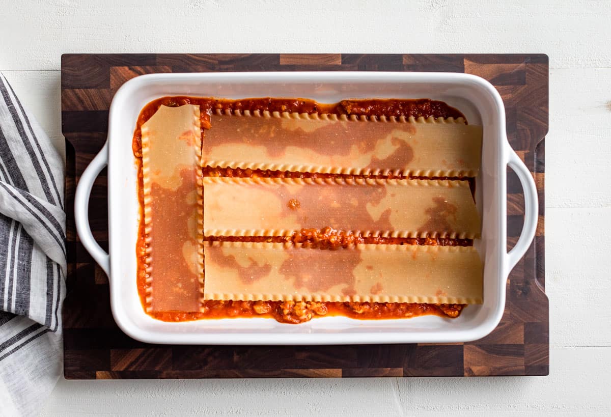 First layer of sauce and lasagna noodles in a white baking dish.