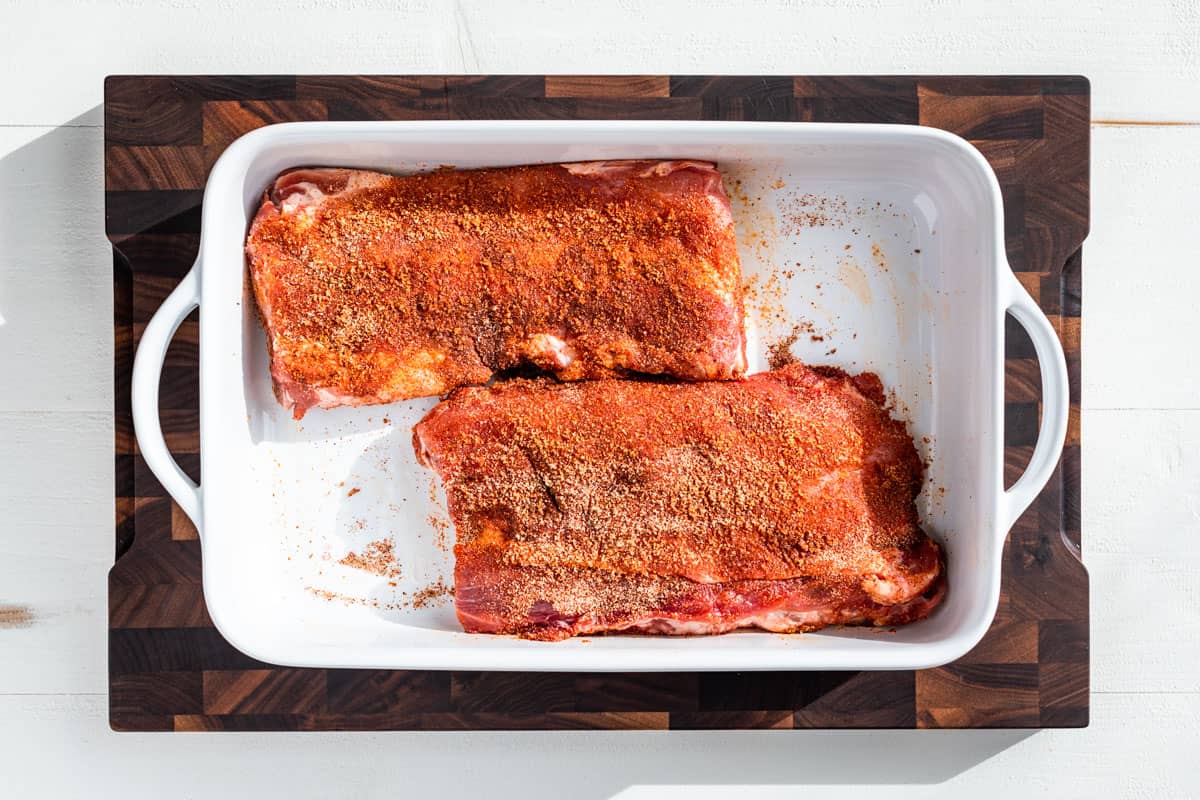 Ribs coated in the spice mixture in a white baking dish.