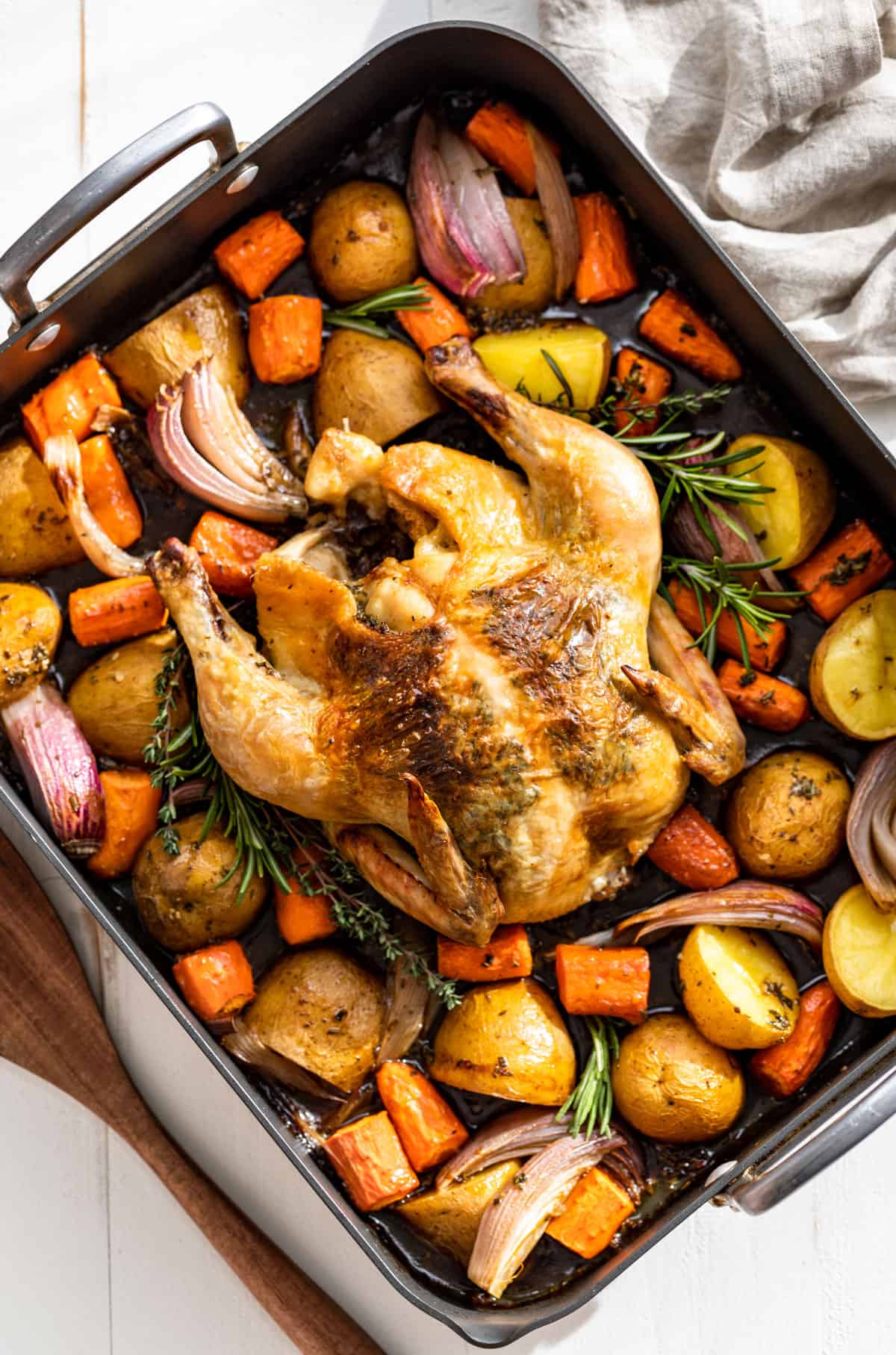 Straight down view of finished Roasted Chicken and Vegetables in a grey roaster with a wooden spatular on the side.