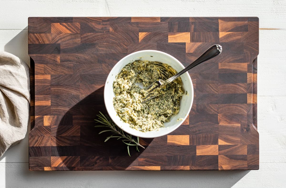 White bowl with chopped rosemary and thyme mashed into butter with minced garlic.