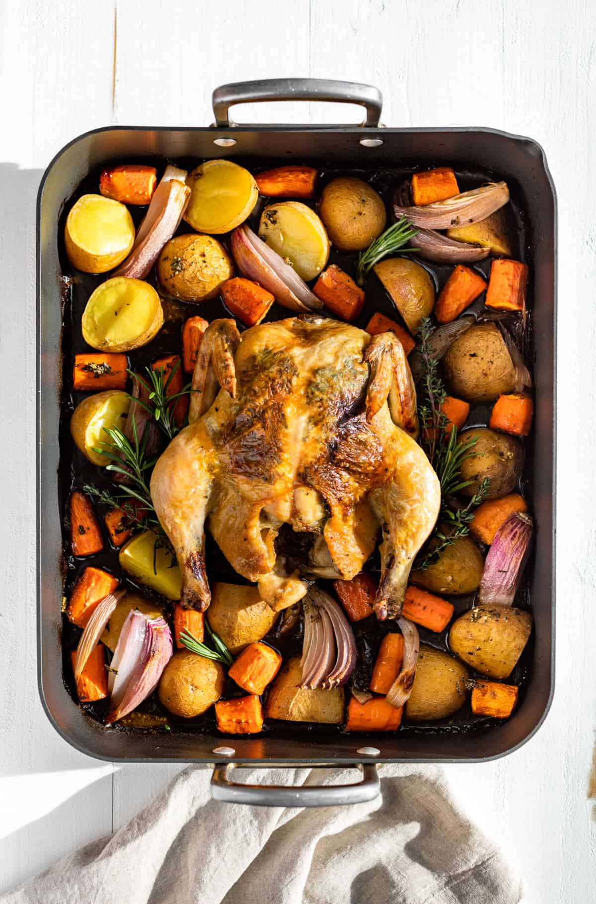 Straight down view of a whole roasted chicken with carrots, potatoes, and onions in a grey roaster.