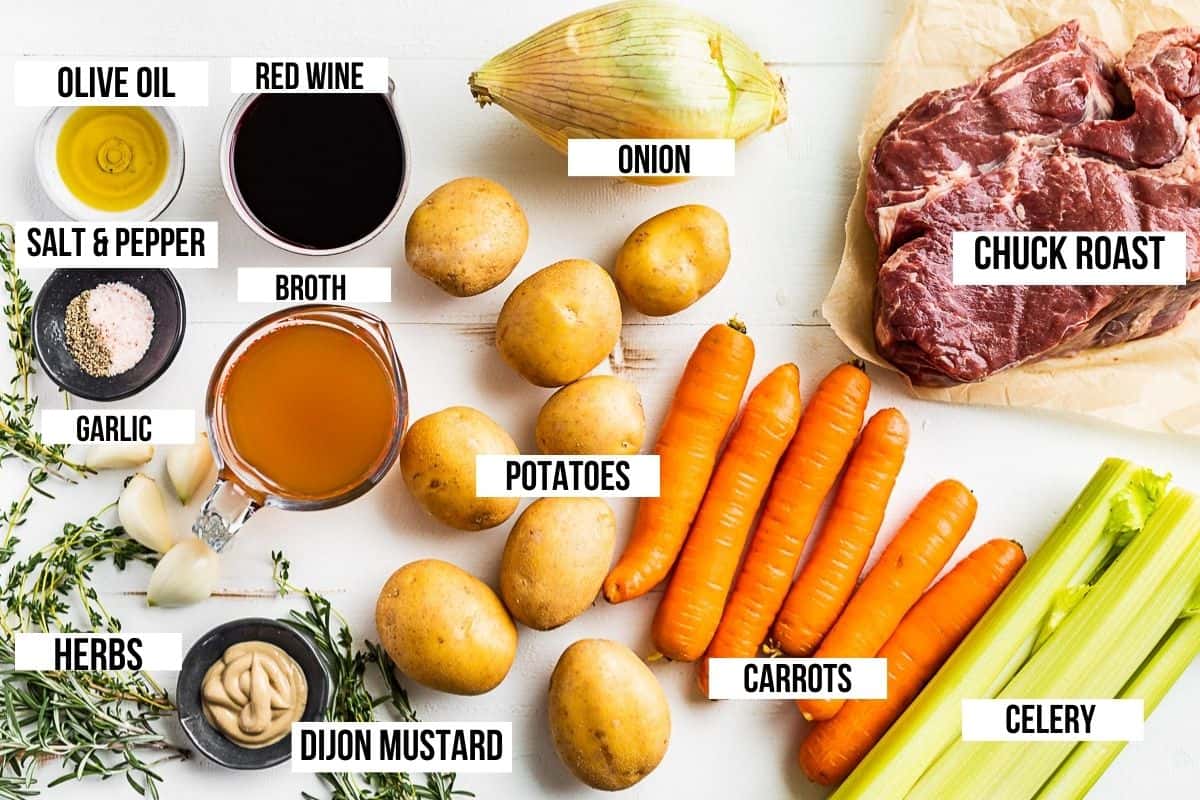 Chuck roast, potatoes, carrots, broth, fresh herbs, onion, celery, and red wine laid on a white board and labeled.