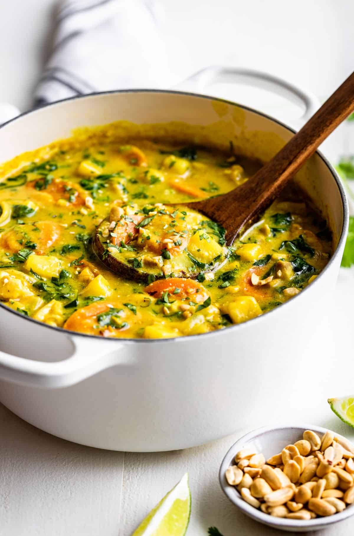 Side view of a white pot filled with yellow curry with a wooden ladle scooping some out.