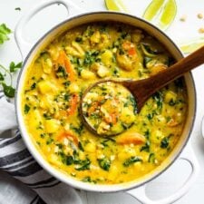 Finished Thai Yellow Curry in a white pot with a wooden ladle and cilantro sprigs.