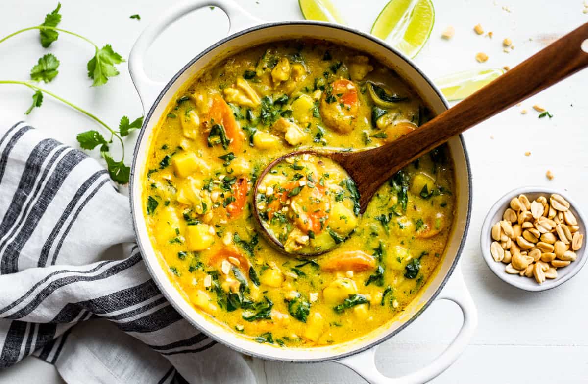 Finished Thai Yellow Curry in a white pot with a wooden ladle and cilantro sprigs.