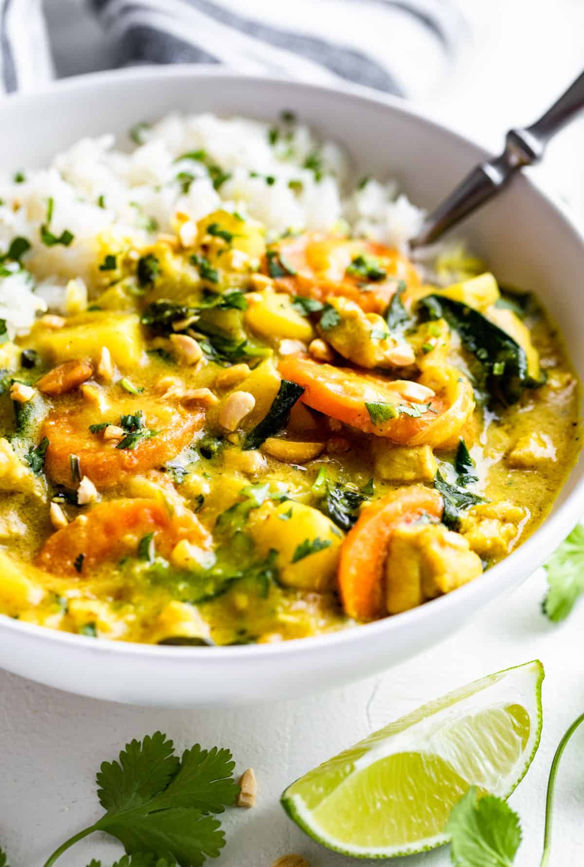 Side view of a white bowl filled with steamed rice and Thai Yellow Curry with chopped cilantro on top.