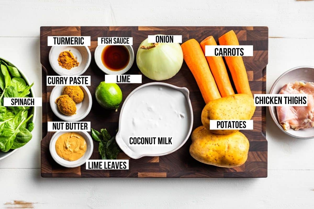 Coconut milk, chicken, carrots, onion, potato, fish sauce, lime leave, and curry paste on a wooden cutting board.