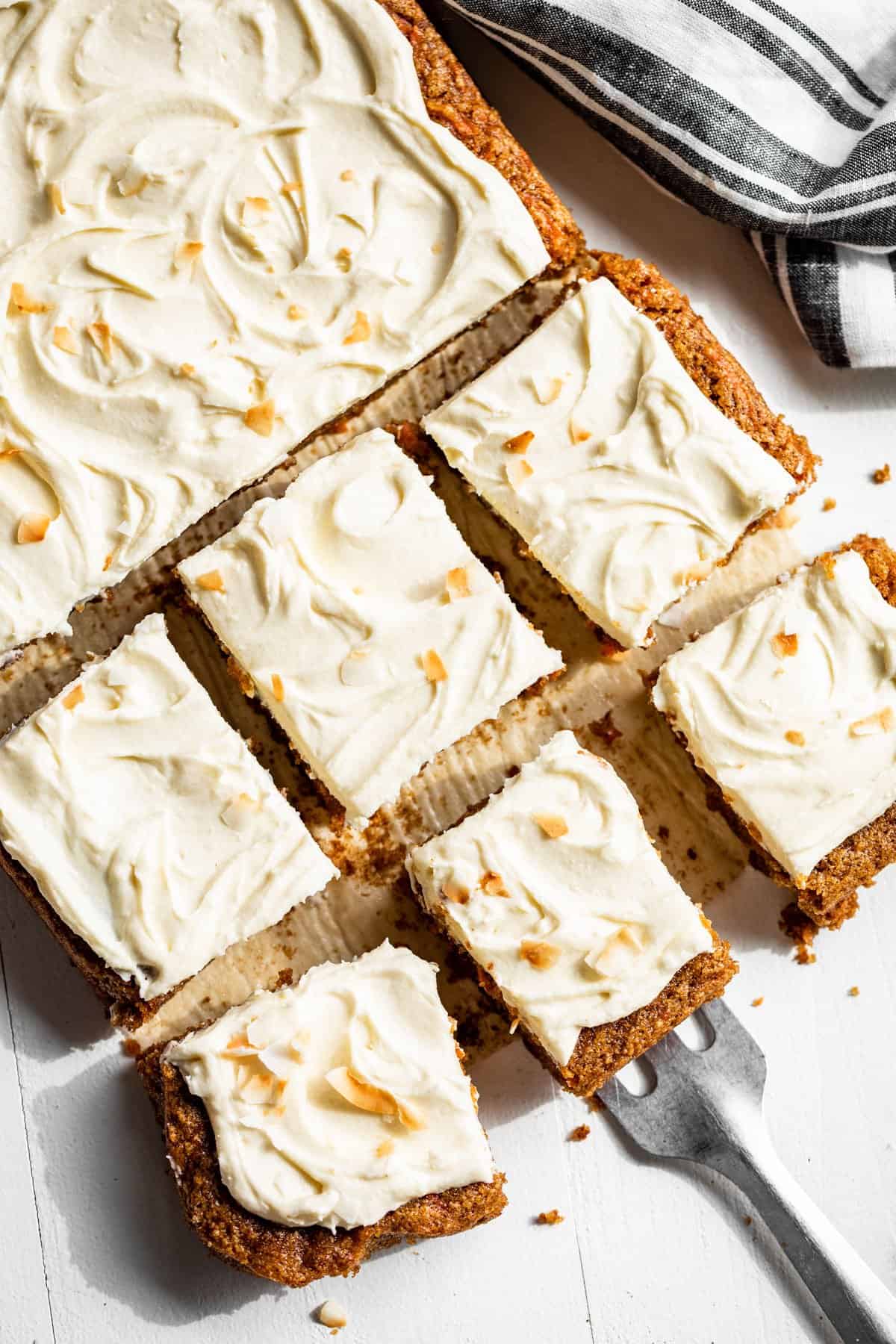 Straight down view of sliced carrot cake with a spatula and a blue striped linen on the side.