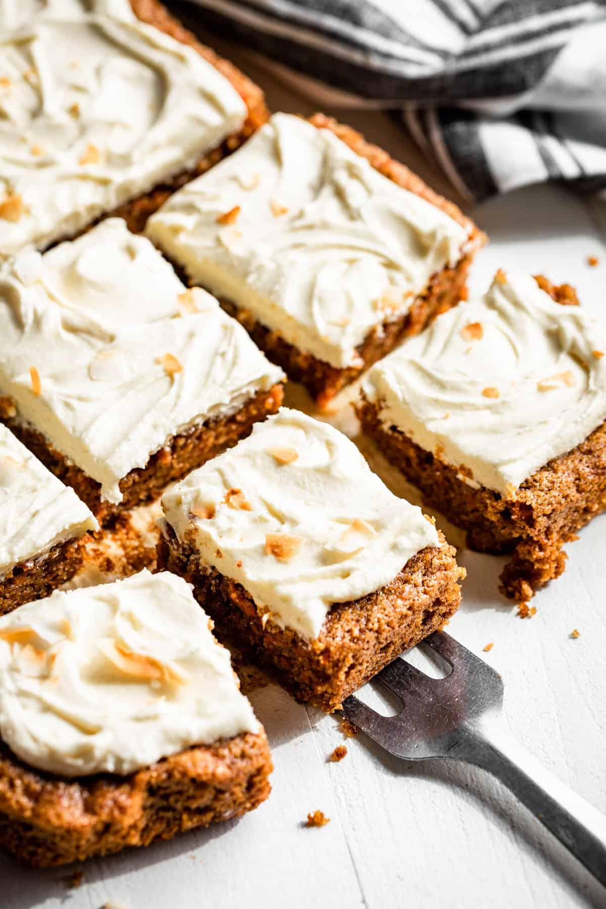 Side view of sliced carrot cake topped with cream cheese frosting with a spatula picking up a piece.