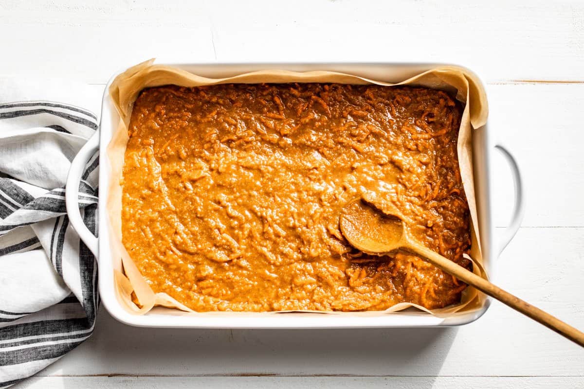 Spreading the carrot cake batter into a prepared baking dish with a wooden spoon.