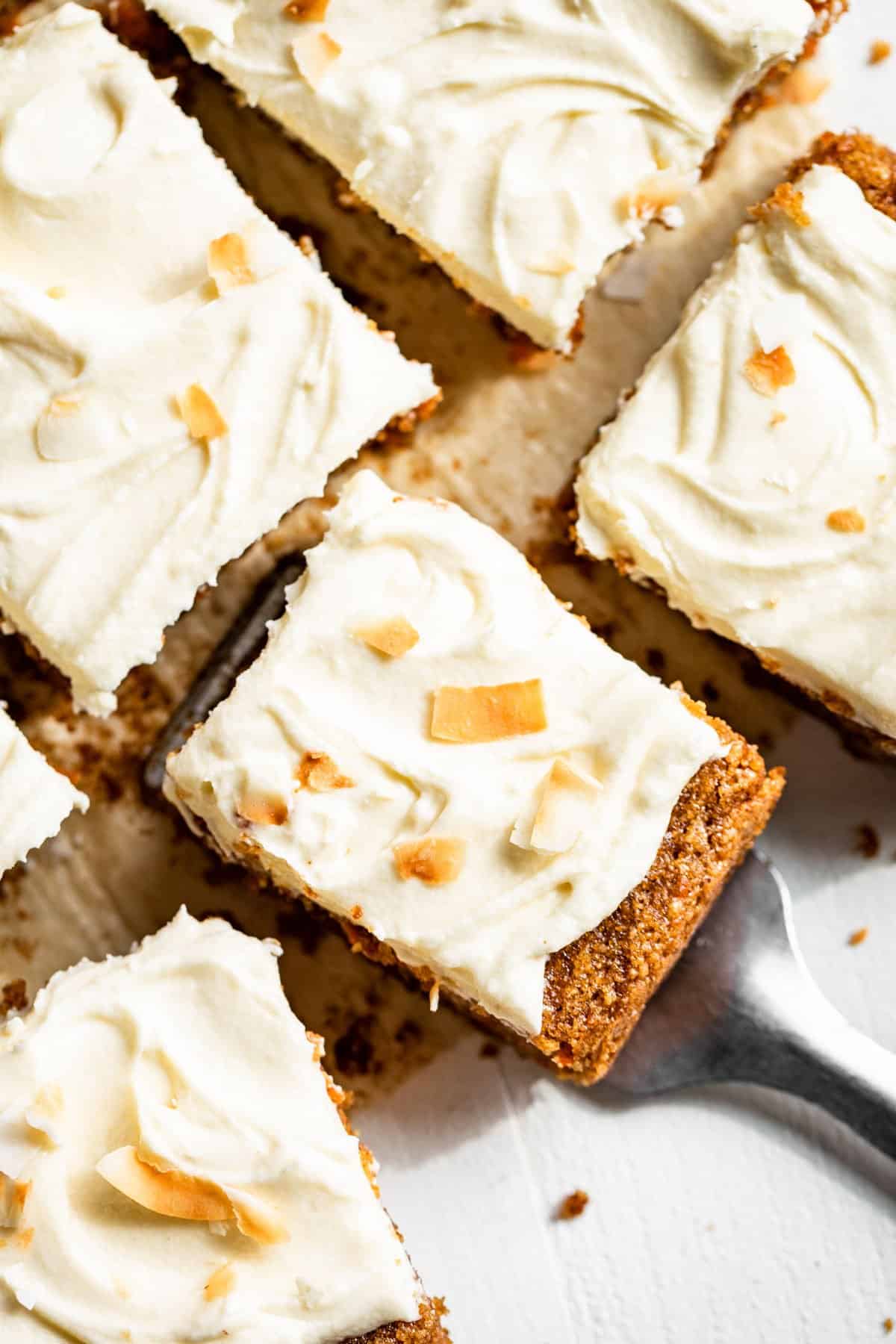 Five slices of carrot cake with a metal spatula lifting out a piece.