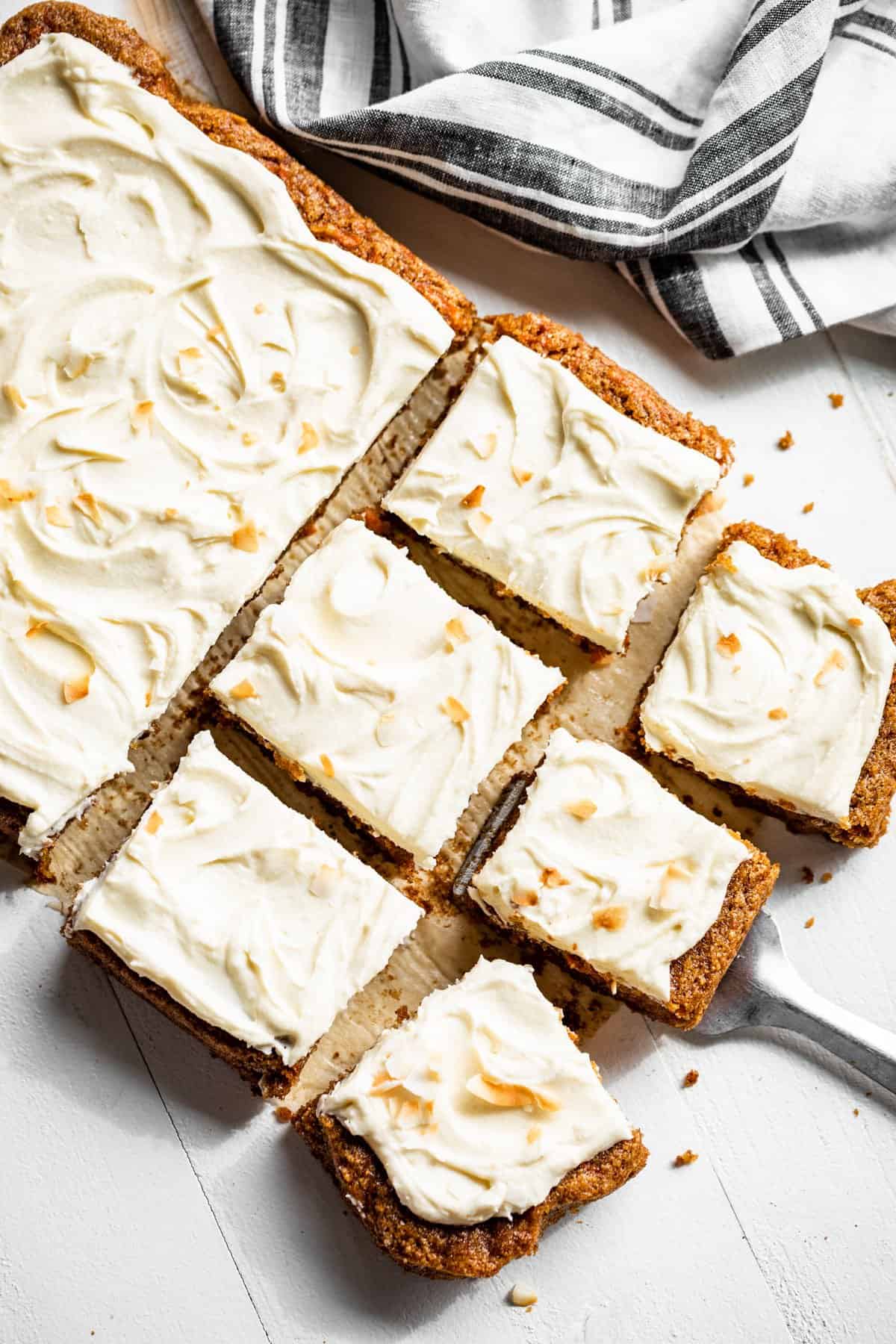 Straight down view of whole carrot cake with six slices cut and a blue striped linen on the side.