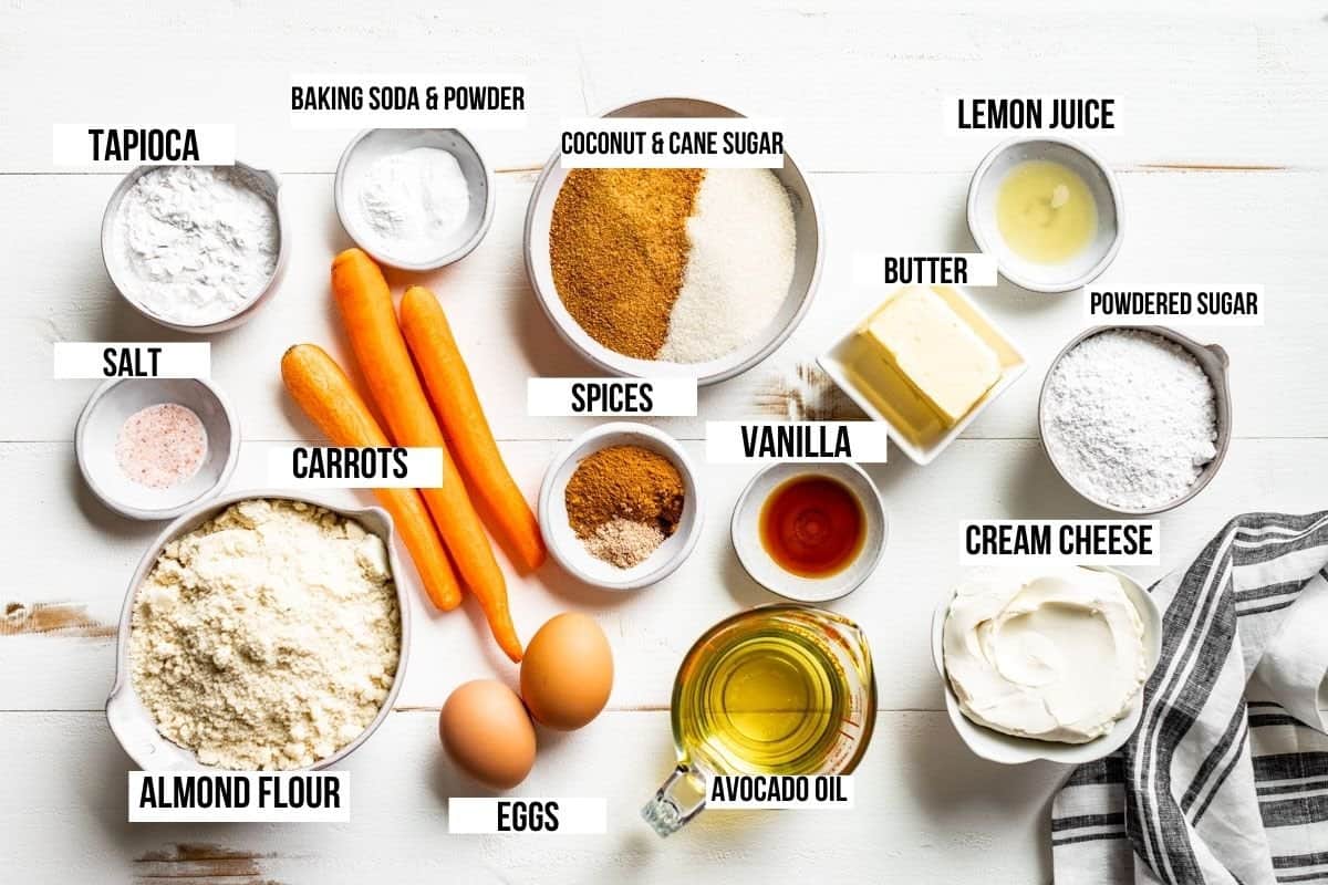 Ingredients for carrot cake in small bowls, almond flour, tapioca starch, sugar, carrots, eggs, avocado oil, cinnamon, cream cheese, butter, and powdered sugar.