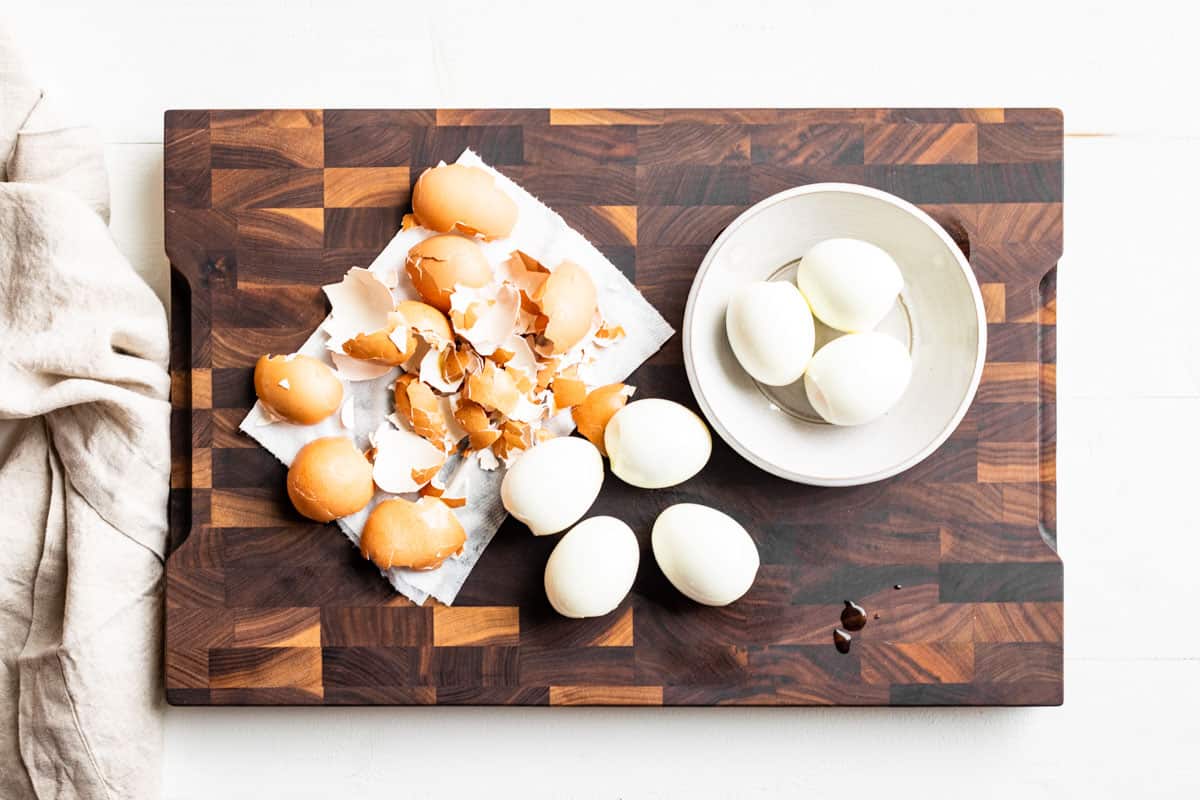 Peeling the hard boiled eggs on a wooden cutting board.