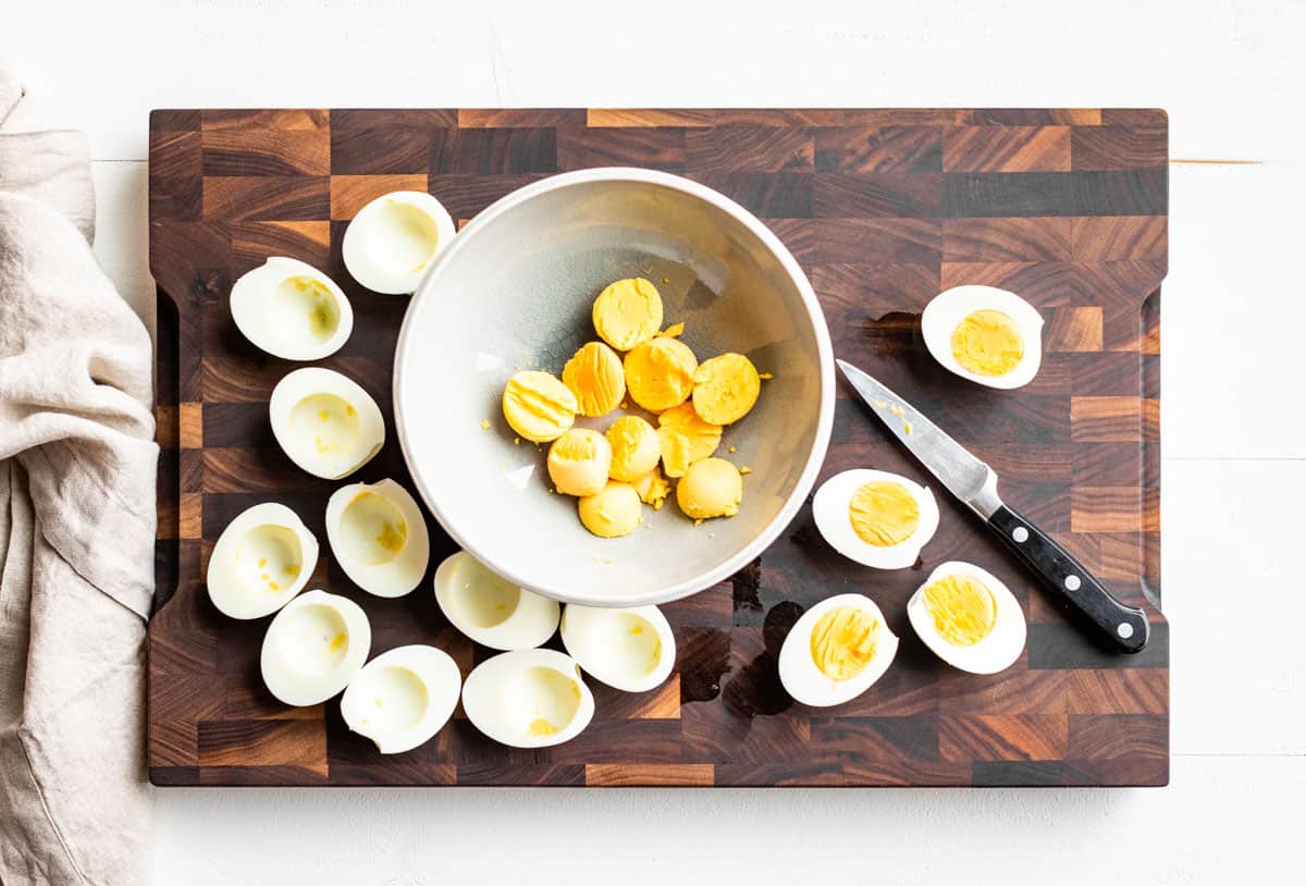 Cutting the hard boiled eggs in half and adding the yolks to a bowl.