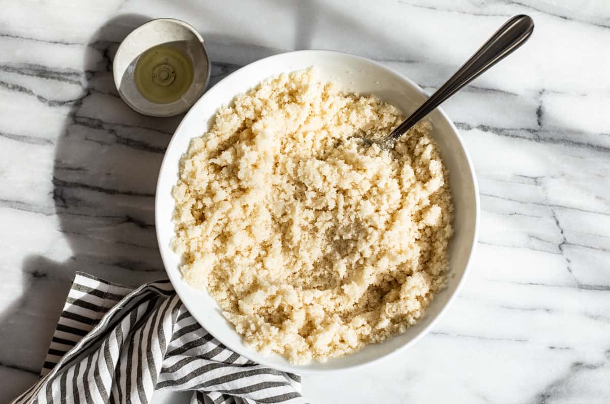 The coconut oil being mixed into the sugar in a large white bowl with a silver spoon.