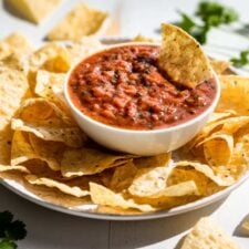 Finished salsa in a white bowl with a corn chip dipping in and corn chips around it.