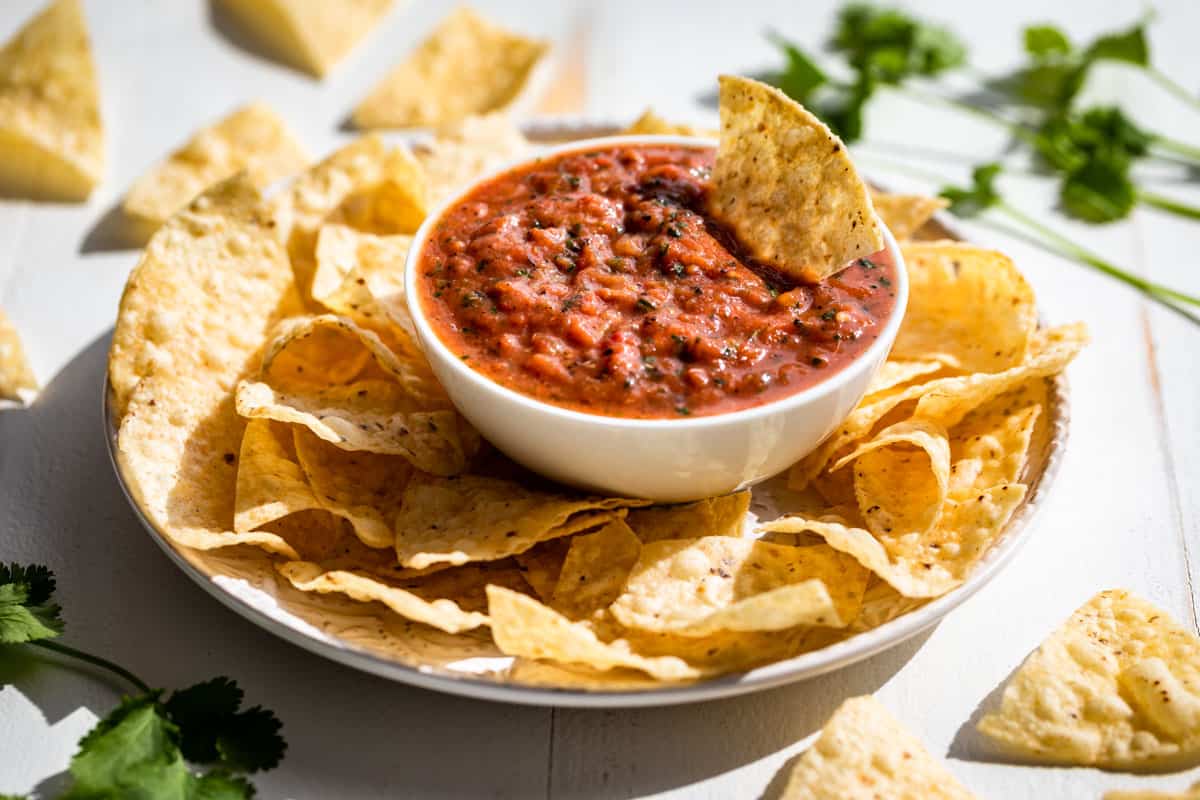 Finished salsa in a white bowl with a corn chip dipping in and corn chips around it.