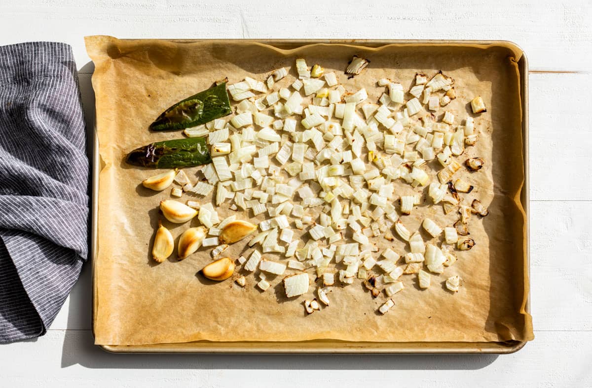 Roasted diced onion, garlic cloves and a halved jalapeno on a wooden cutting board.