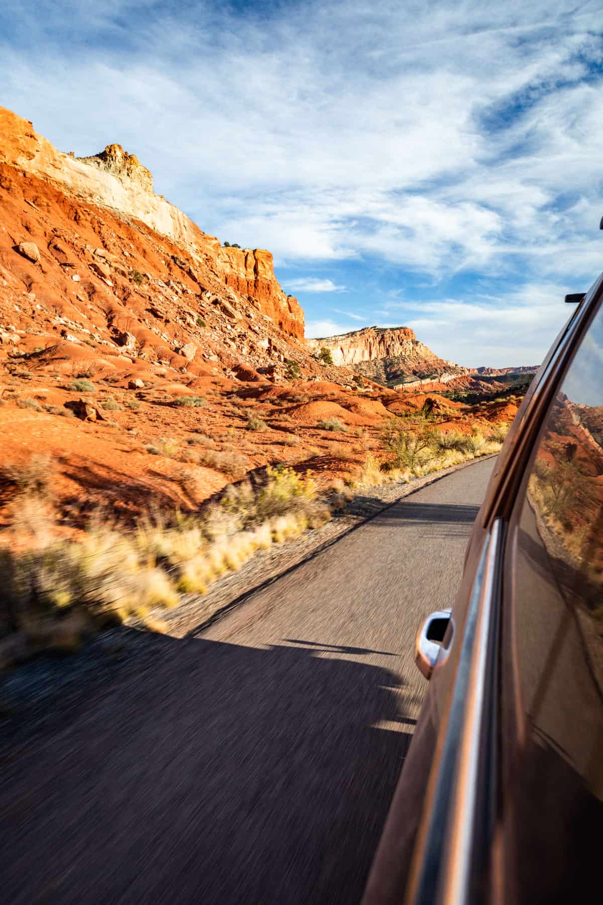 View looking back out of the passenger side of a black truck of the orange walls of rock by the scenic byway in Capitol Reef.