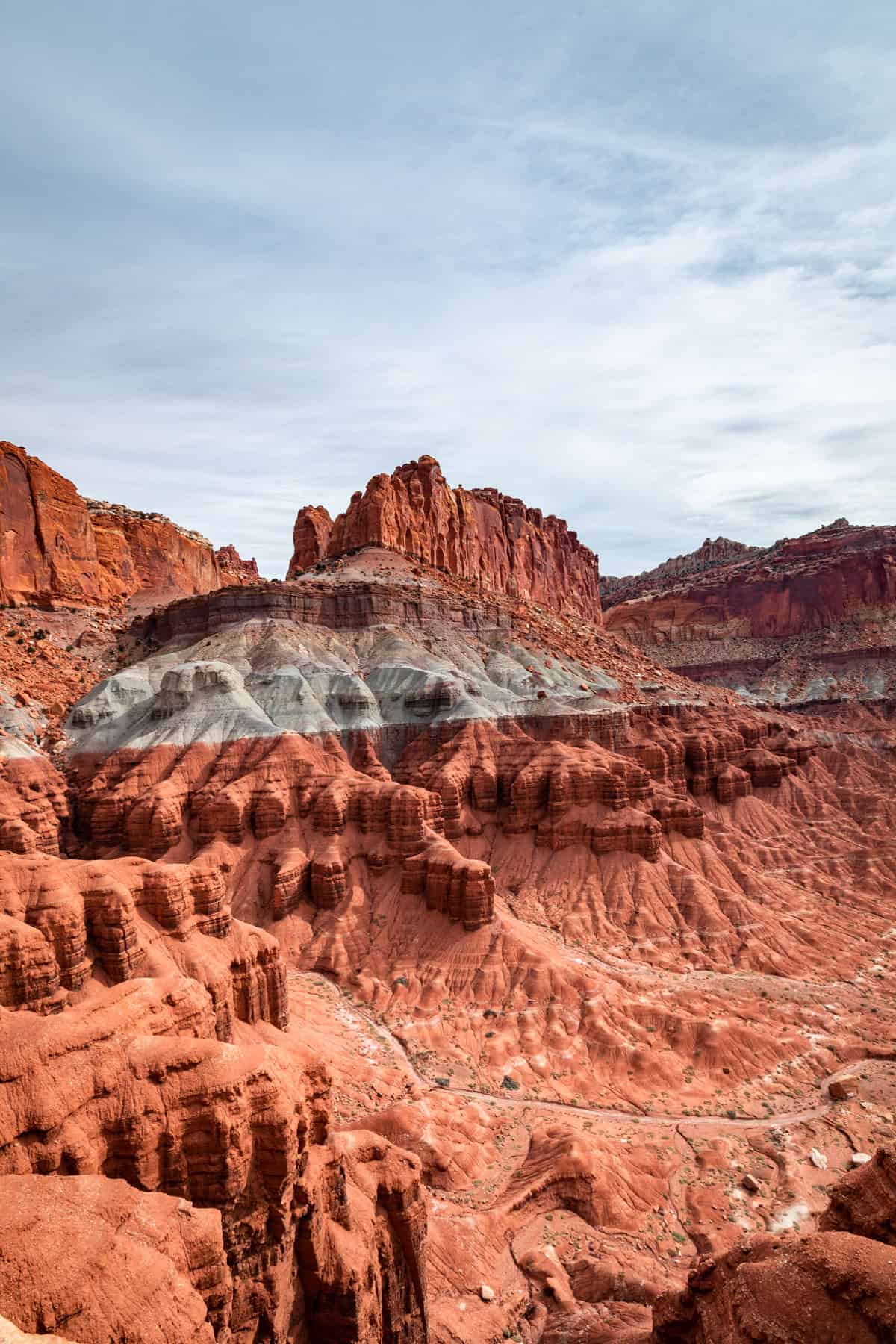 Red rock formations with a blueish stripe in the middle and blue skies with scattered clouds.